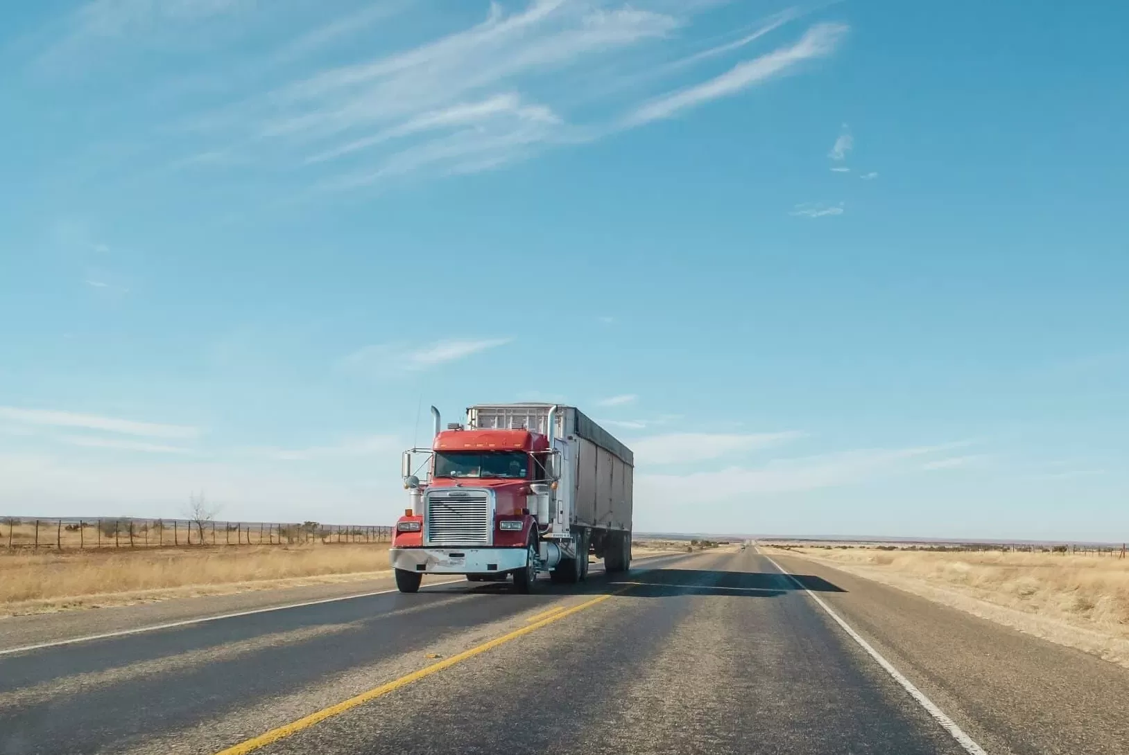 A red Freightliner truck with a trainer on the road