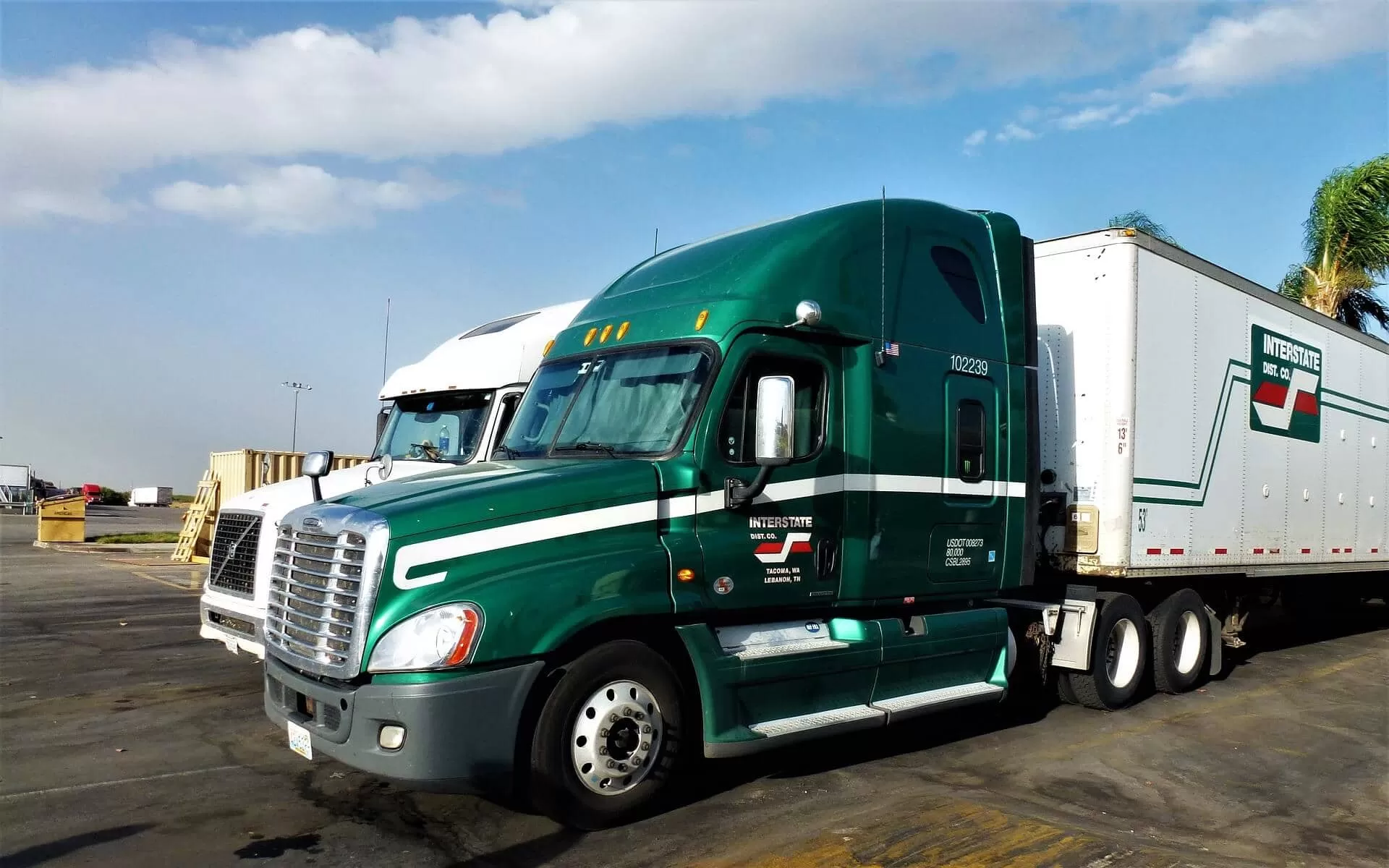 Green truck Freightliner with white trailer on the truck parking