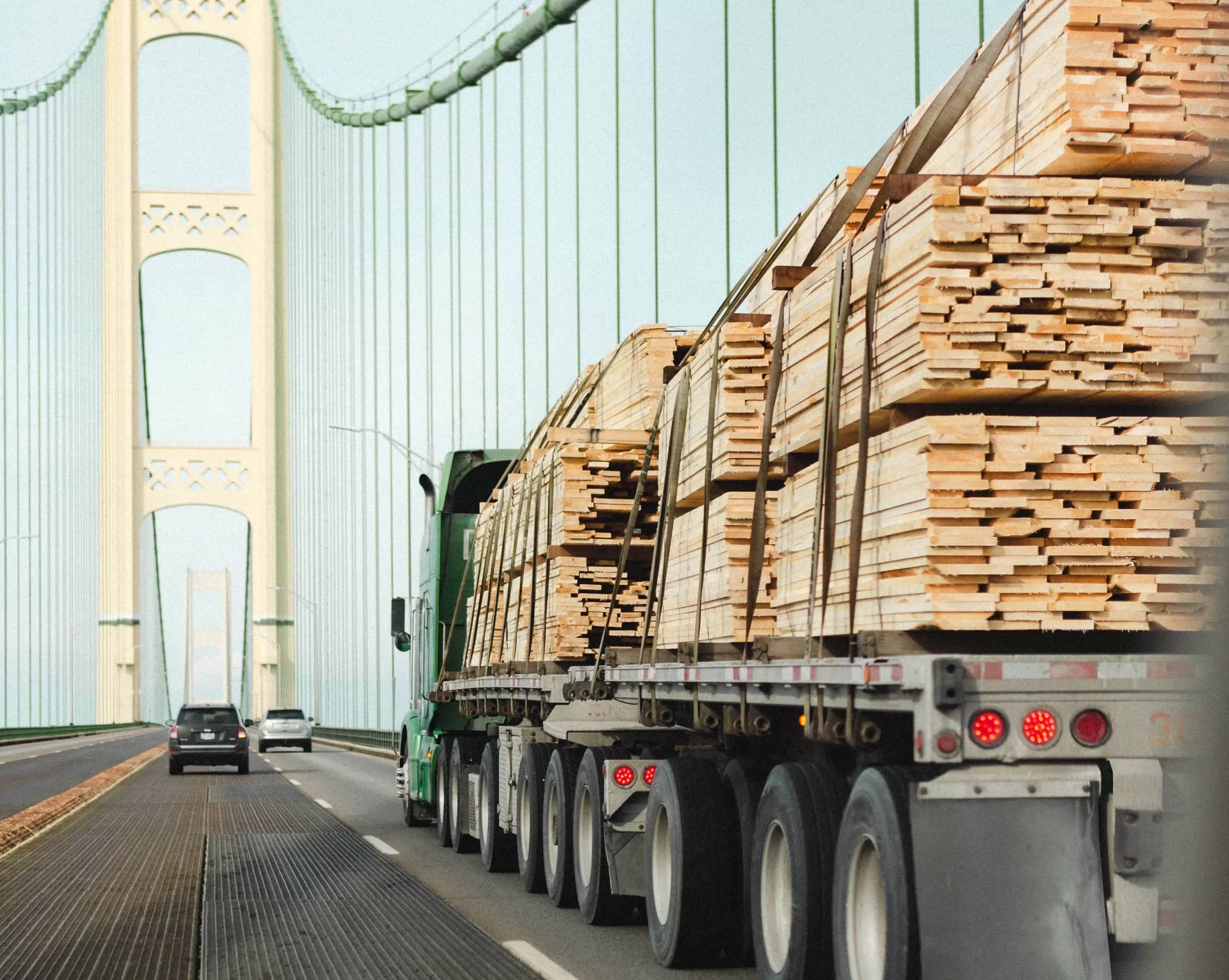 A green truck on the bridge loaded with wood