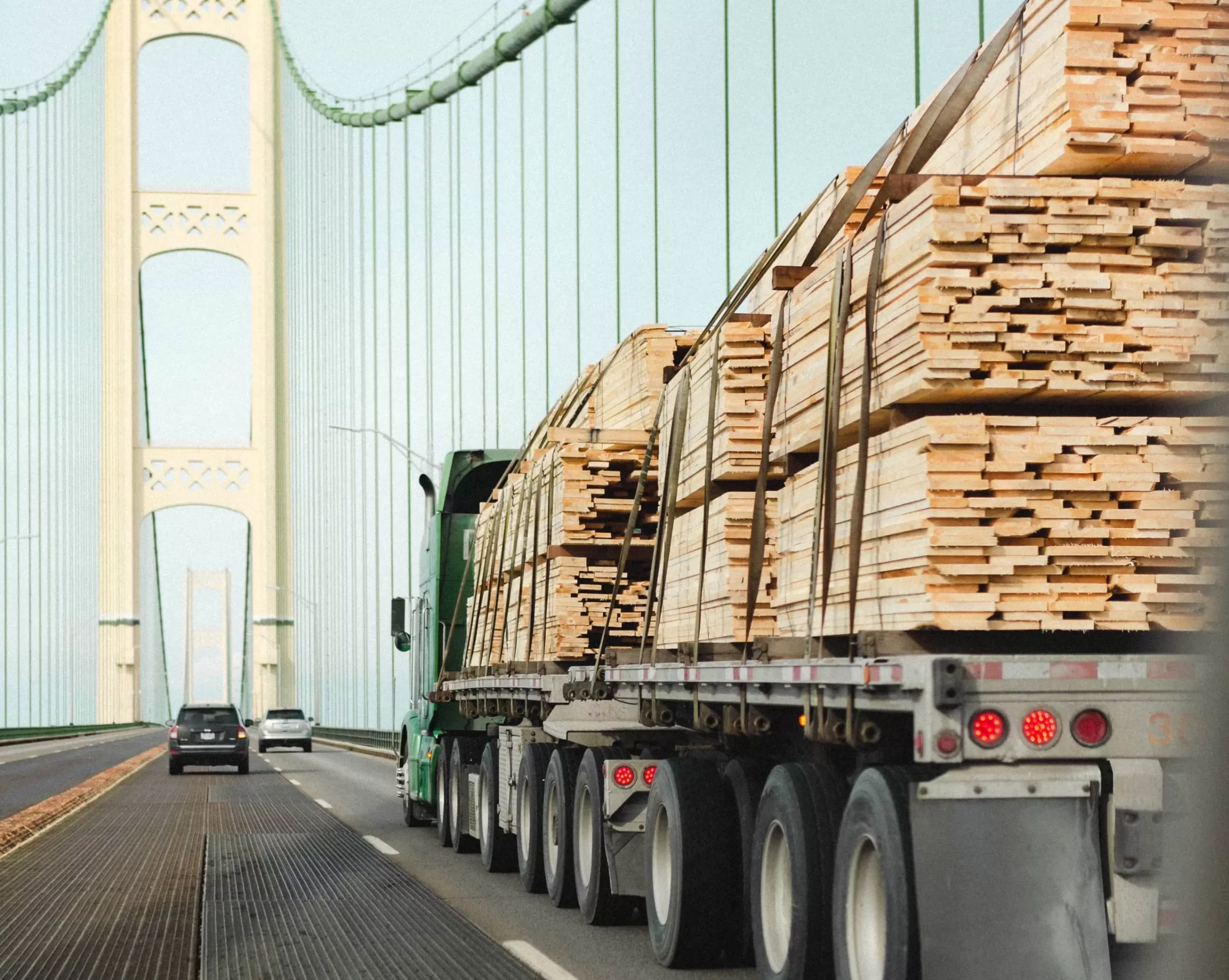 a green truck on the bridge loaded with wood scaled